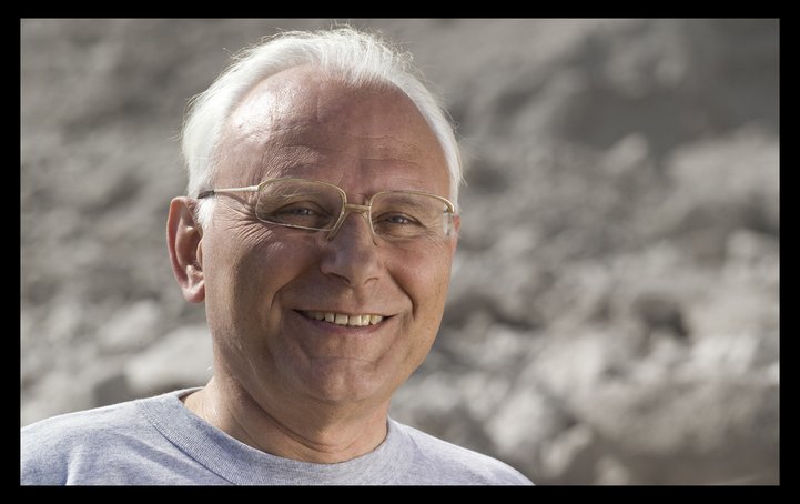 Porträtfoto eines Mannes mit grauen, kurzen Haaren, Brille und freundlichem Lächeln.
