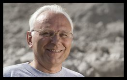 Porträtfoto eines Mannes mit grauen, kurzen Haaren, Brille und freundlichem Lächeln.