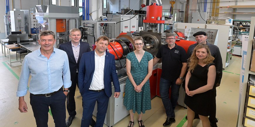 Gruppenfoto mit 7 Personen vor einer neuen metallenen Anlage in der einer großen Laborhalle.