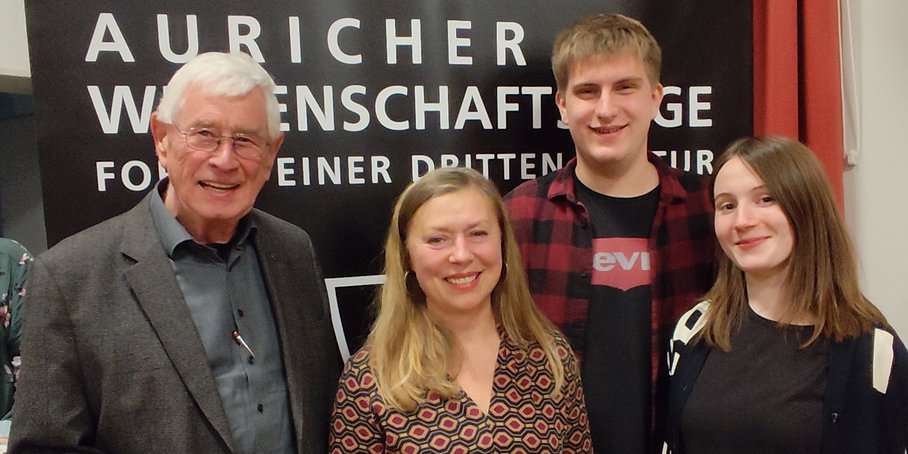 Group photo with four people in front of a dark wall with the words “Auricher Wissenschaftstage”