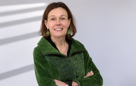 Portraitfoto mit grauem lichtdurchfluteten Hintergrund, vor dem Körper verschränkte Arme