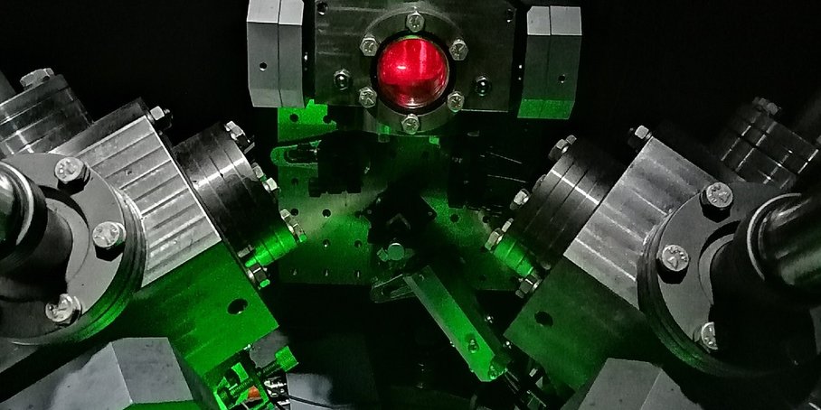 An assembly of metal components and flanges with thick bolts. The foreground is bathed in green light. Red light can be seen through a small round window.