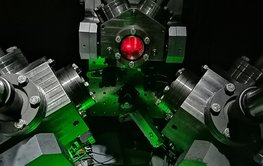 An assembly of metal components and flanges with thick bolts. The foreground is bathed in green light. Red light can be seen through a small round window.