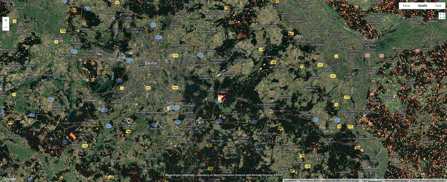 A satellite image of a landscape with labelling of streets and localities, featuring many small patches in various shades of green. Interspersed among them are splashes of white, yellow, orange and red, which are much more frequent and denser on the eastern side of the image – in Poland.