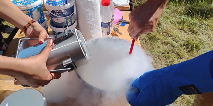 Auf einem Tisch wird mit flüssigem Stickstoff Eis selbstgemacht. Hände, Schüssel, und es qualmt.