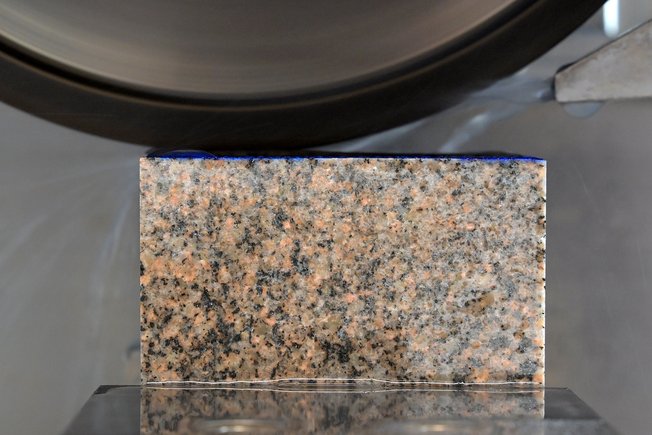 Ein Gesteinswürfel von 80 Millimeter Breite wird mit einem runden Schleifkopf unter einem Flüssigkeitsstahl geschliffen.
