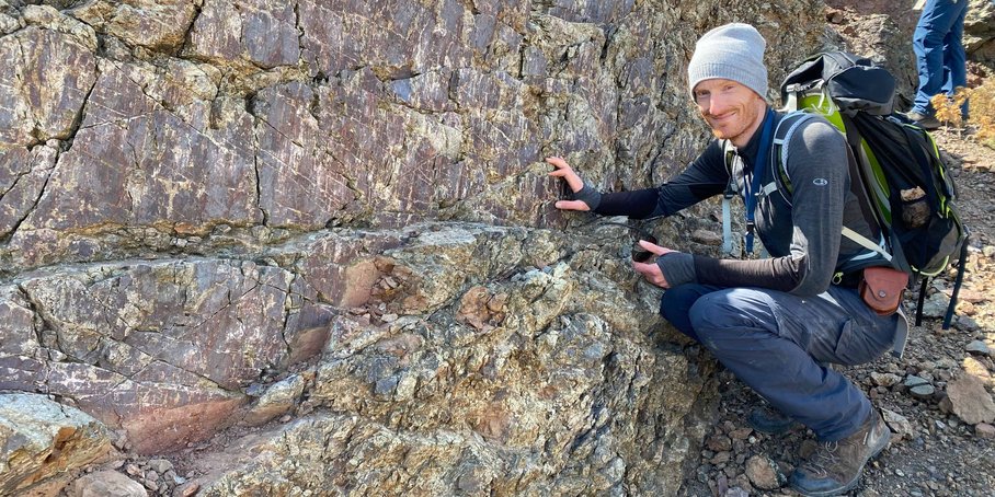 Ein junger Mann hockt neben einem verwitternden Felsen.