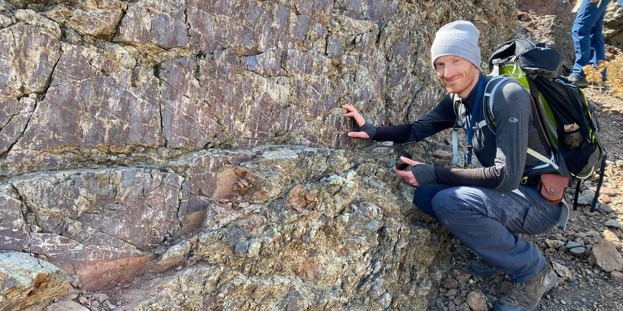 A young man crouches next to a weathered rock.