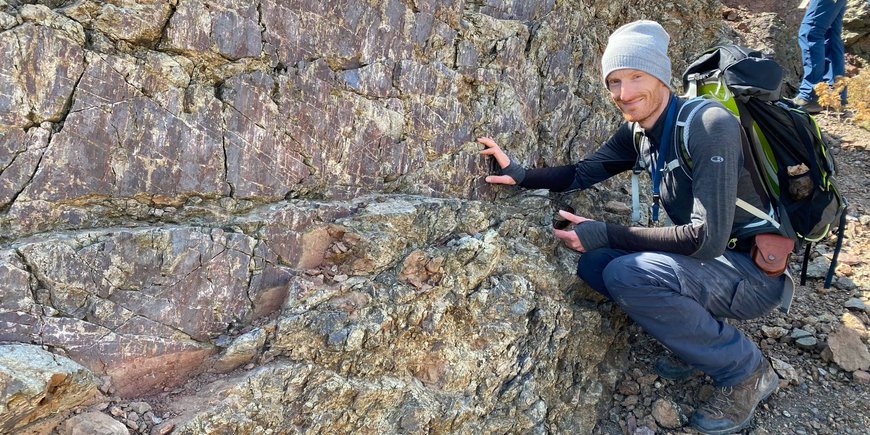 Ein junger Mann hockt neben einem verwitternden Felsen.