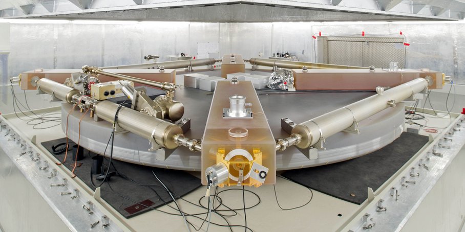 In a laboratory, metal tubes are arranged in a square pattern on a circular disc. There are also cables, control units and measuring instruments.