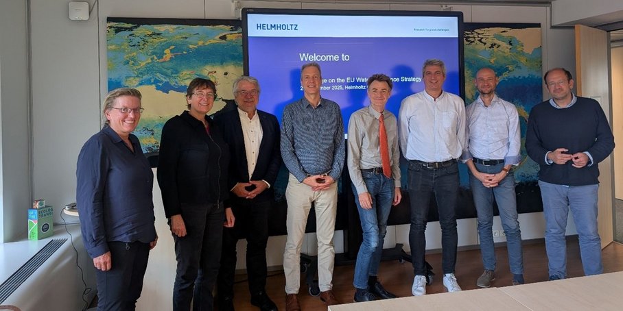 Gruppenfoto mit 8 Personen in einem Seminarraum vor einer Leinwand.