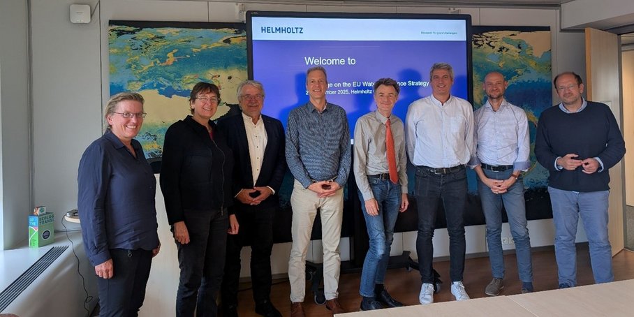 Group photo with 8 people in a seminar room in front of a screen.