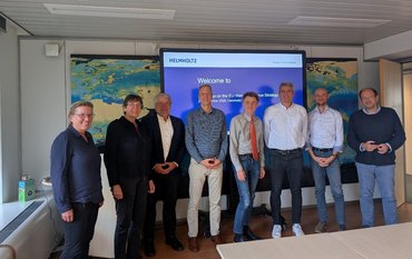 Gruppenfoto mit 8 Personen in einem Seminarraum vor einer Leinwand.