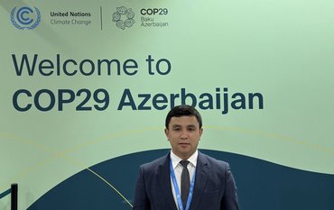 Abror Gafurov von dem Schriftzug "Welcome to Azerbaijan" und den UN und COP Logos
