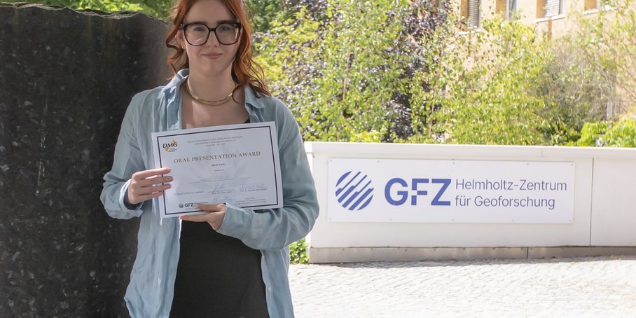 The picture shows Candice Filoche holding the DMG award in her hands. In the background, you can see a column from the Column Forum and the GFZ logo at the entrance to House G.