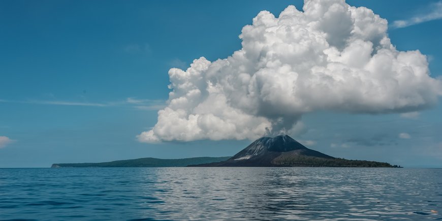 Insel-Vulkan mit Aschewolke, im Vordergrund ist ein ruhiges Meer zu sehen
