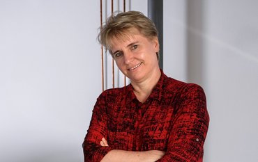 Profil von Prof. Dr. Liane G. Benning, mit kurzen blonden Haaren, rotem Oberteil und Lächelndem Blick