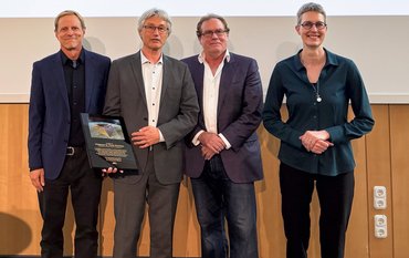 Einfaches Gruppenbild vor einer Wand von vier Personen frontal.