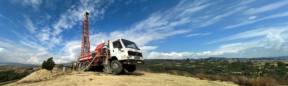 Lorry with approx. 10-metre-high drilling rig in a barren, hilly landscape against a blue sky with streaks of clouds