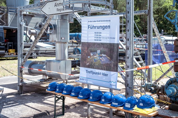 An einem Metallgerüst hängt ein Plakat, das Führungen ankündigt. Davor sind blaue Schutzhelme aufgereiht.