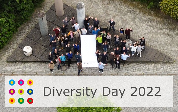 Eine Gruppe von Menschen steht um die Flagge des Diversity Day versammelt - im Säulenforum auf dem Telegrafenberg