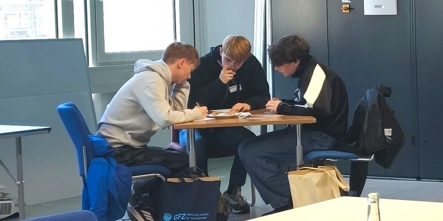 Drei Schüler sitzen konzentriert um einen runden Tisch und bearbeiten eine Aufgabe.