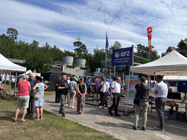 Menschen stehen in Grüppchen, im Hintergrund Zelte und technische Anlagen.