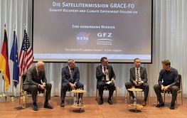 panel discussion Panel discussion of five people in front of a screen. On the side a German, European and American flag each