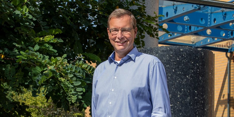 Porträt eines Mannes im mittleren Alter vor grüner Vegetation und Steinsäulen. Im Hintergrund ein GFZ-Logo.