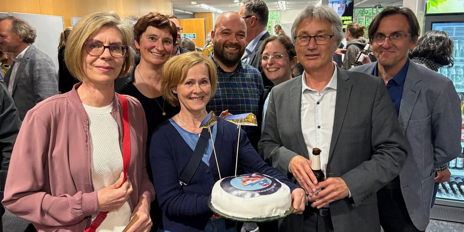 Group photo of six people facing the camera with a decorated GRACE cake.