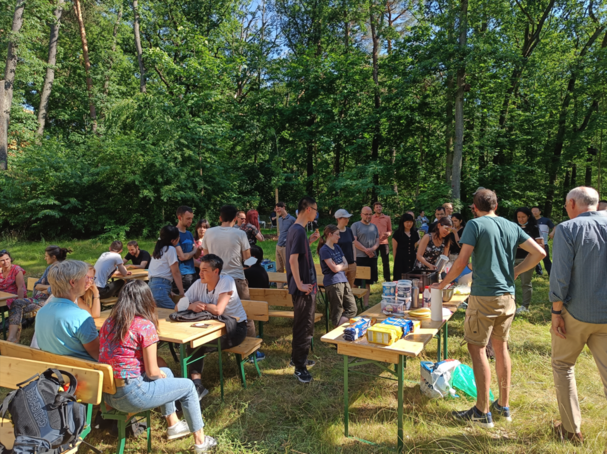 Eine Gruppe Menschen sitzt auf Bänken im Grünen und sie essen Eis