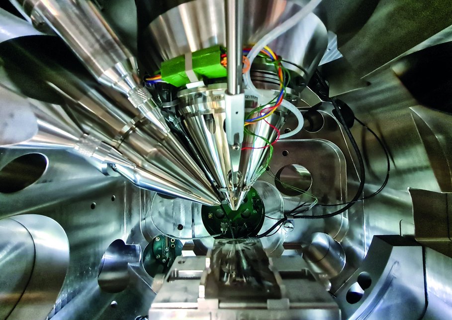 View into the sample chamber of our dual-beam electron microscope, that look like converging metallic cylinders.