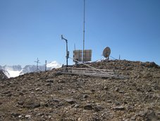 Die Abbildung zeigt die ROMPS am Abramov Gletscher. Im Vordergrund steht ein Schneemesssystem. Dahinter von rechts nach links, die GPS-Antenne, Solarzellen und der Windmast, ein Regensammler und links ein Strahlungssensor und ein Temperaturmessgerät.