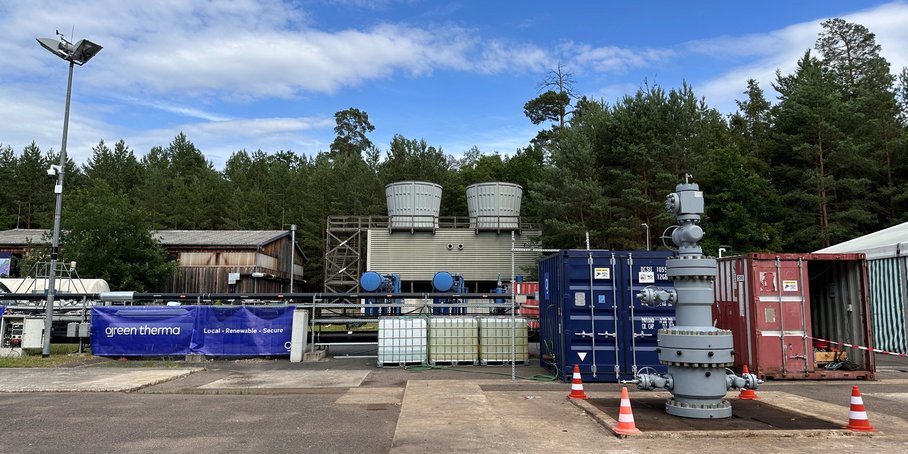 Metallcontainer, Metallrohre, davor ein Betonplatz. Im Hintergrund Kühlanlage.