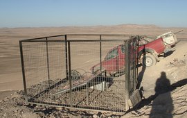 Das Foto zeigt eine umzäunte Solaranlage in einer staubigen Landschaft. Es steht ein Auto hinter dem Zaun