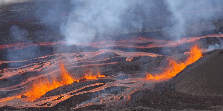 Red lava streams on black background. In the front we see red sparkling lava, the air is filled with smoke.