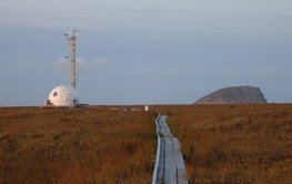 Links ein Messturm in niedrig bewachsener Tundralandschaft.