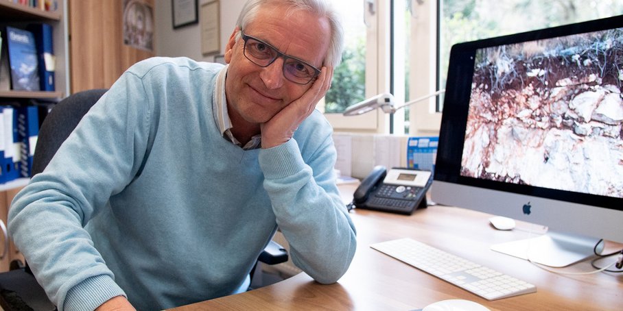 Friedhelm von Blanckenburg sitting, leaning on the table. Computer in the backround.