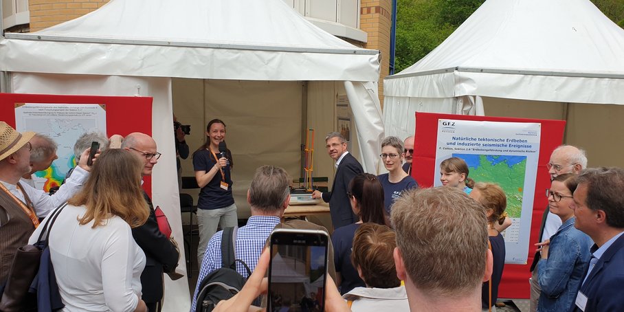 Eine Gruppe Menschen steht an einem weißen Veranstaltungszelt. Eine Frau spricht in eine Mikrofon.