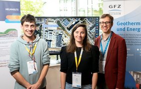 Gruppenfoto mit drei jungen Menschen vor einer Posterwand
