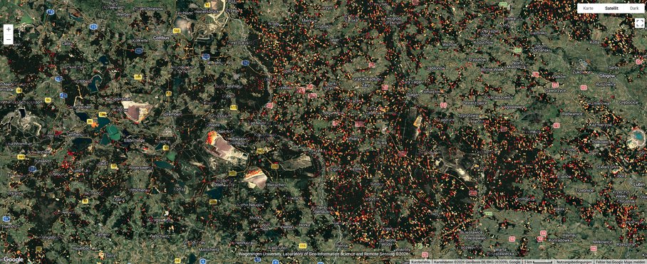 A satellite image of a landscape with labels for streets and localities, featuring many small patches in various shades of green. Interspersed among them are splashes of white, yellow, orange and red, which are much more frequent and denser on the eastern side of the image – in Poland.