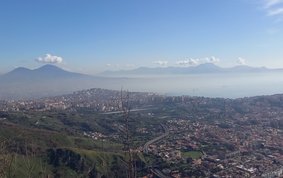 Städtisches Gebiet am Fuße eines Berges, im Hintergrund weitere Berge und das Meer.