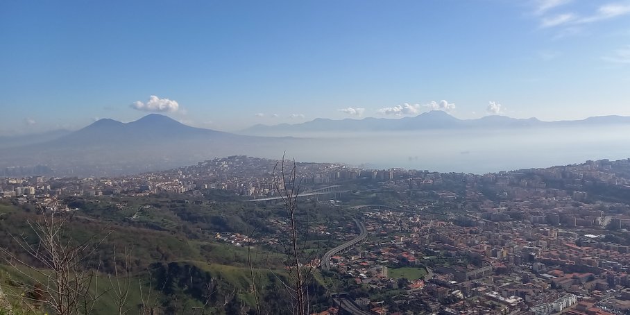 Städtisches Gebiet am Fuße eines Berges, im Hintergrund weitere Berge und das Meer.