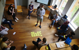 People sit on chairs in a circle in a room.