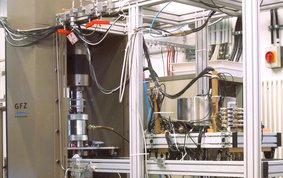 Szene im geomechanischen Hochdrucklabor: Metallgestell mit metallenen Behältern, Kabeln, Messgeräten und einer Presse.