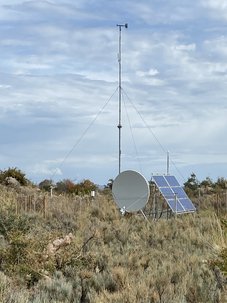 Das Bild zeigt eine ROMPS Installation. Im Vordergrund ist die VSAT-Antenne zu sehen, dahinter der Windmast. Rechts davon die Solarpanele für die Stromerzeugung. Links steht ein Regensammler und eine GNSS-Antenne.