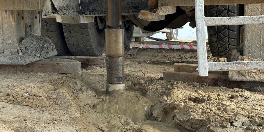Blick auf das Bohrgeschehen unter dem LKW: Rund um das im Bohrloch sich drehende Gestänge ist hellbraune schlammige Flüssigkeit.