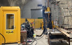Eine ca. 10 Meter hohe Tiefbohranlage steht in einem Untertage-Tunnel, daneben ein Gerüst, Leitungen und weiteres Gerät sowie eine gelbe, telefonzellengroße Steuerkabine.