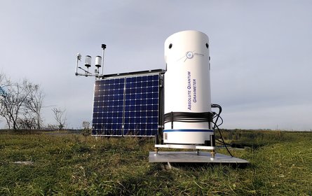 On a green field stands a white, barrel-shaped container with an inscription, in which the sensitive measuring device is installed. Next to it is a solar panel.