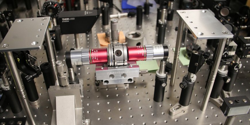 Ein Laser-Tisch im Labor: Auf eine metallische Platte sind viele Linsen und andere optische Elemente geschraubt. In der Mitte ist die Handtteller-große metallene Diamant-Stempel-Zelle.